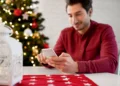 Homem usando smartphone em ambiente natalino com árvores de Natal e luzes brilhantes, perfeito para mensagens de fim de ano.