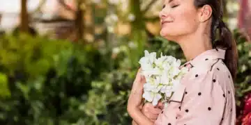 Mulher em contato com flores brancas em um jardim, representando o bem-estar emocional proporcionado por plantas que florescem no verão.