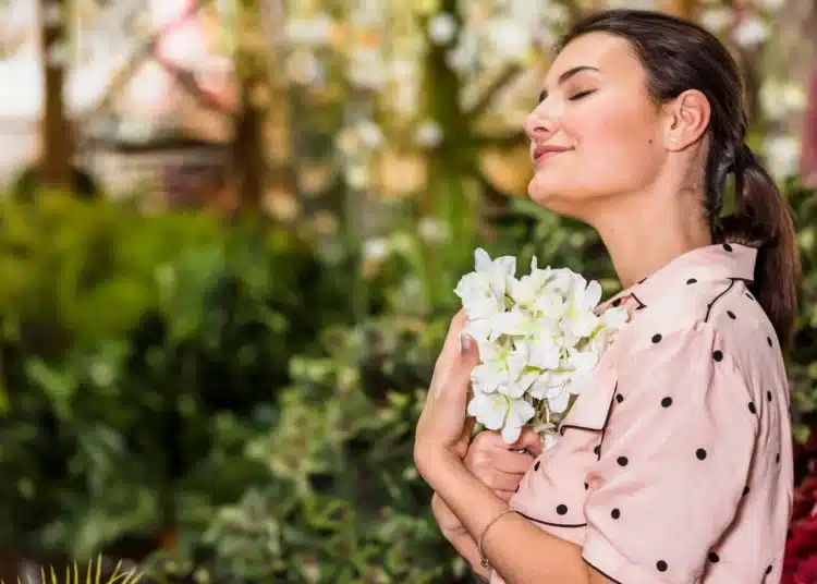 Mulher em contato com flores brancas em um jardim, representando o bem-estar emocional proporcionado por plantas que florescem no verão.