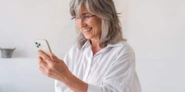Mulher sorridente e elegante lendo mensagens de boa noite no seu smartphone, em um momento de gratidão e fé antes de dormir.