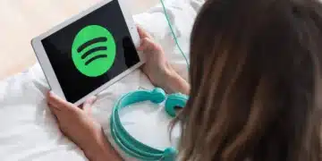 Pessoa utilizando tablet com o logo do Spotify enquanto prepara fones de ouvido, representando a divulgação dos álbuns mais ouvidos de 2025.