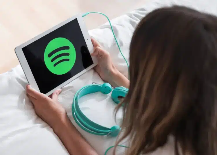Pessoa utilizando tablet com o logo do Spotify enquanto prepara fones de ouvido, representando a divulgação dos álbuns mais ouvidos de 2025.