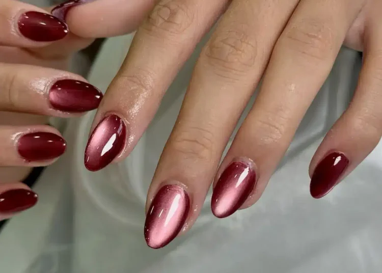 Unhas em gel decoradas com esmalte vermelho metálico em formato amendoado, com efeito ombré de vermelho escuro a claro.