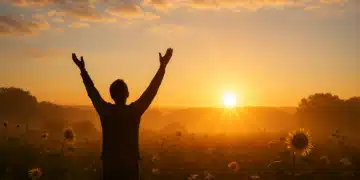 Pessoa de braços erguidos em um campo ao nascer do sol.