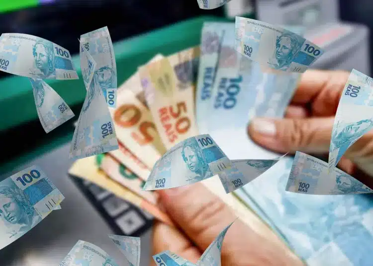 Diversas cédulas de 100 reais e algumas de 50 reais voando em frente a uma pessoa segurando dinheiro