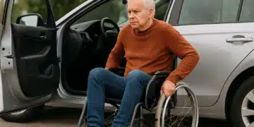 Idoso em cadeira de rodas ao lado de carro.