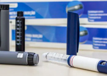 Canetas de emagrecimento cinza e branca sobre superfície com embalagens azuis ao fundo