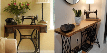 Máquina de costura Singer antiga de pedal com a base de ferro trabalhada e um tampo de madeira, transformada em um aparador com vaso de flores, luminária e telefone retrô.