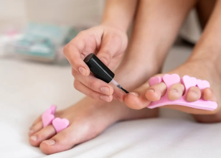 Mulher aplicando esmalte nos pés com separadores de dedos rosas, representando tendências de pedicure de 2026.
