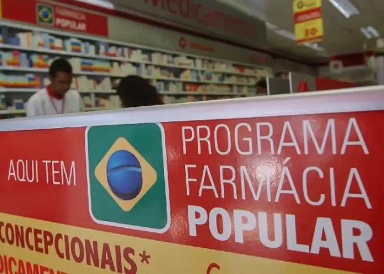 Cartaz do Programa Farmácia Popular em farmácia com prateleiras e atendentes ao fundo