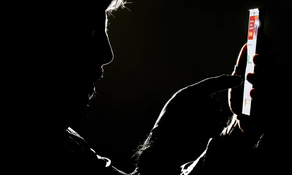 Homem usando smartphone em ambiente escuro Silhueta de homem mexendo no celular iluminado em fundo preto