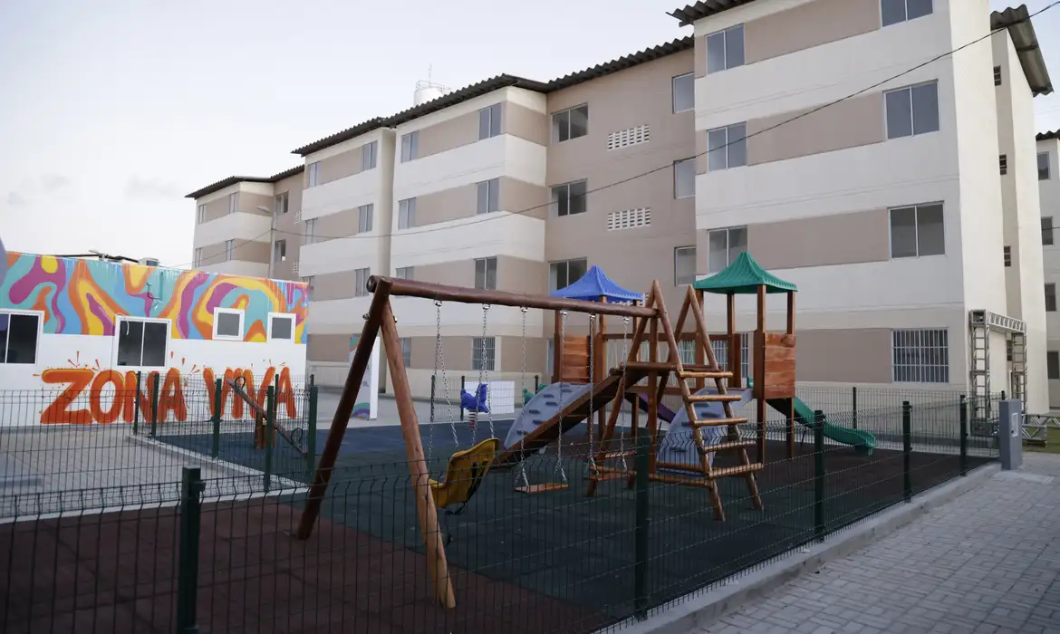 Condomínios populares com área de lazer infantil Playground cercado em condomínio residencial popular com prédios ao fundo