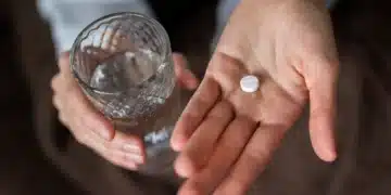 Pessoa segurando pílula e copo de água, com foco no medicamento para queima de gordura.