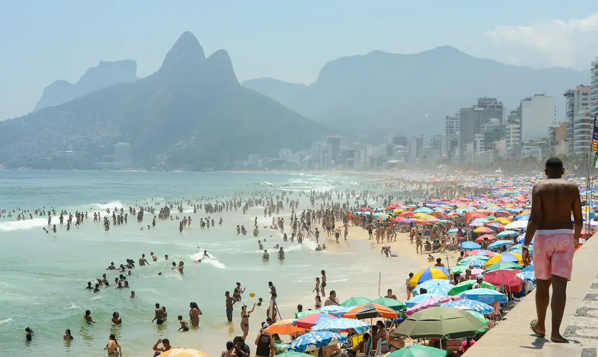 Praia de Ipanema lotada com vista para Dois Irmãos Praia de Ipanema cheia de banhistas e guarda-sóis coloridos com montanhas Dois Irmãos ao fundo