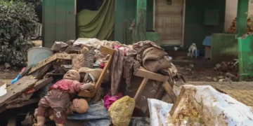 Amontoado de pertences cobertos de lama em frente a uma casa, boneca suja à vista, 2026