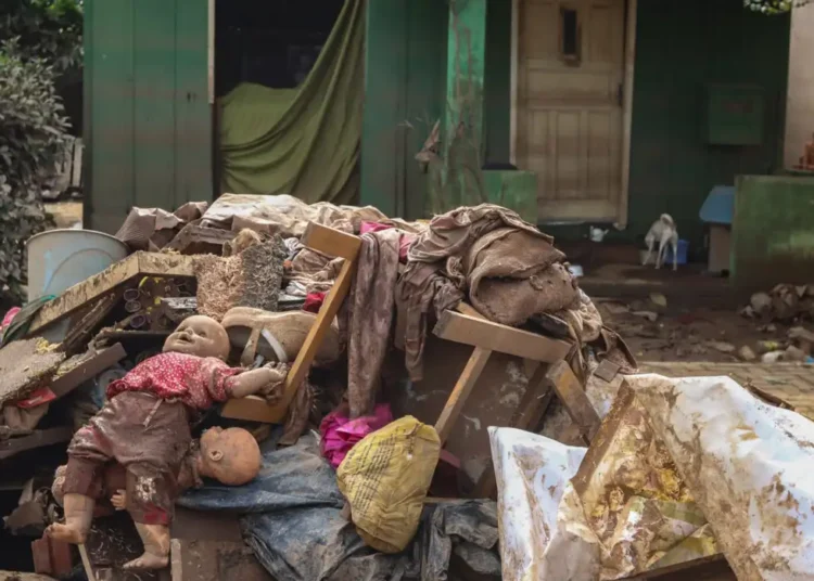 Amontoado de pertences cobertos de lama em frente a uma casa, boneca suja à vista, 2026