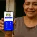 Mulher sorridente mostrando smartphone com aplicativo Bolsa Família em frente à casa
