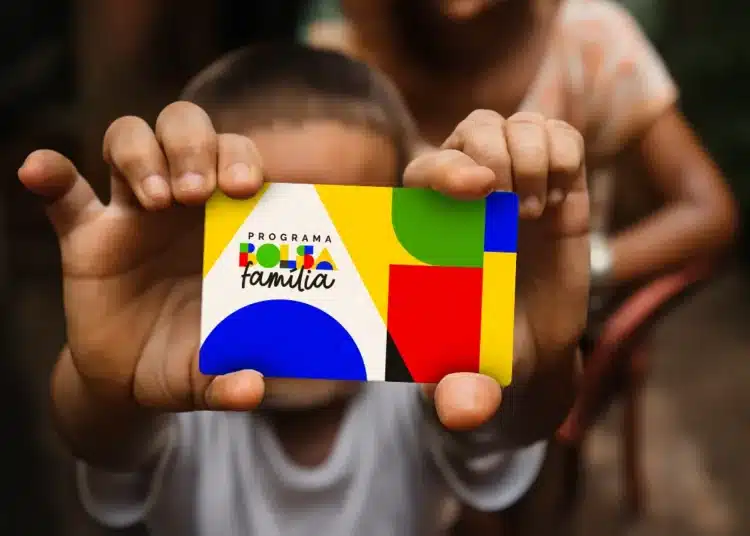 Criança segurando cartão do Bolsa Família colorido em primeiro plano