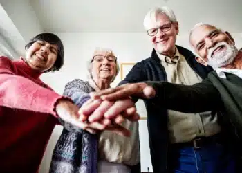 Grupo de idosos com mãos unidas, simbolizando colaboração e apoio mútuo.