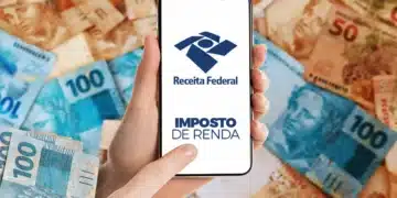 Mão segura celular com logo da Receita Federal sobre notas de real espalhadas