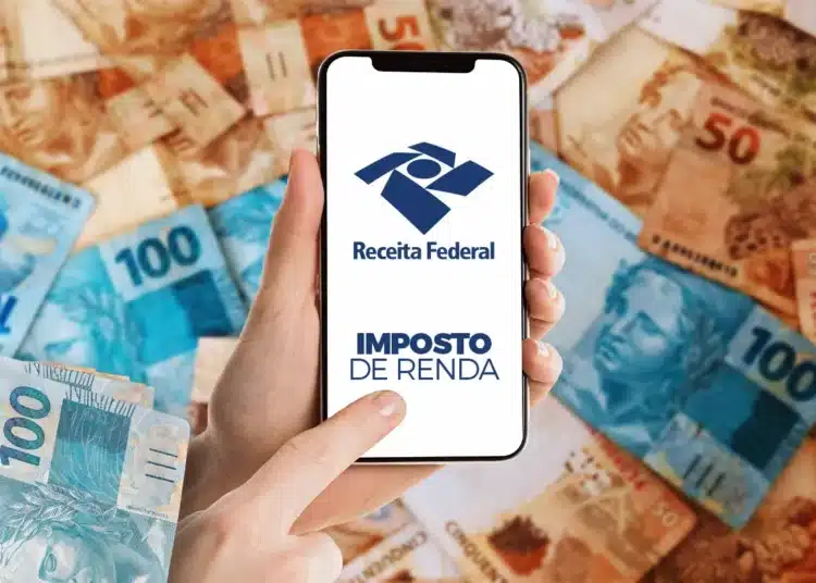 Mão segura celular com logo da Receita Federal sobre notas de real espalhadas
