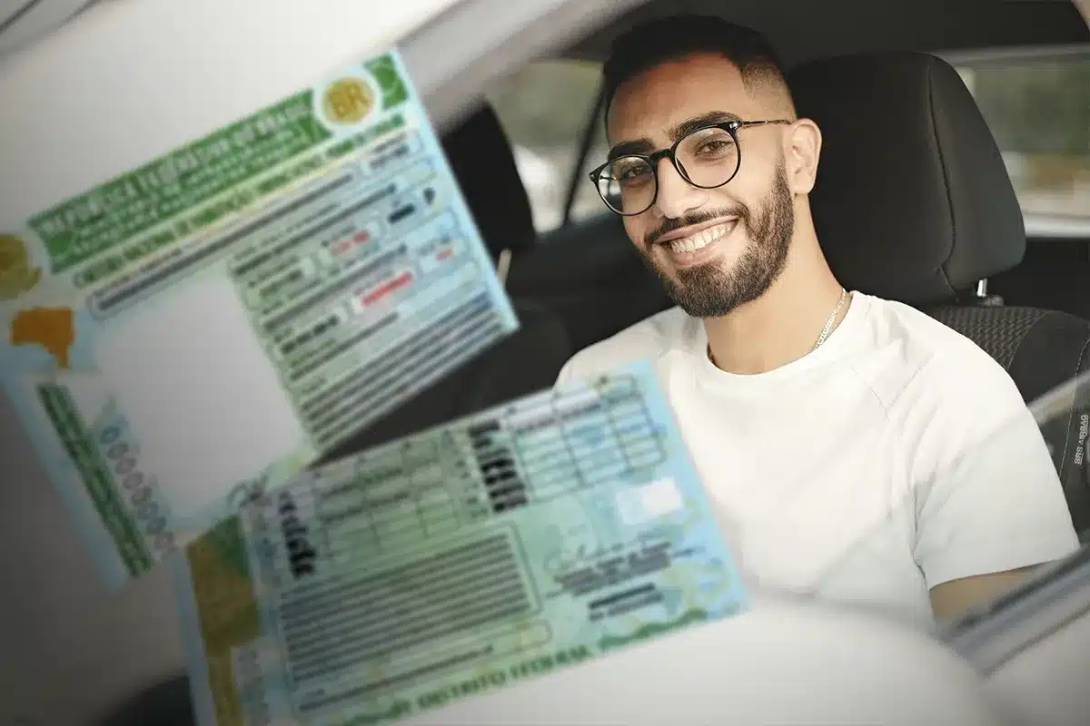 Mudanças na CNH. Homem sorrindo mostra carteira de motorista dentro do carro.
