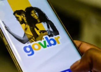 Pessoa segura smartphone exibindo tela do aplicativo gov.br com imagens de duas pessoas sorrindo