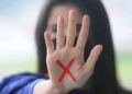 Mulher com a mão estendida exibindo um X vermelho como símbolo de combate à violência contra a mulher