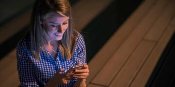 Mulher sorridente em camisa xadrez digitando no celular iluminado à noite