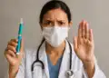 Profissional de saúde com máscara mostra caneta injetável e faz sinal de pare com a mão