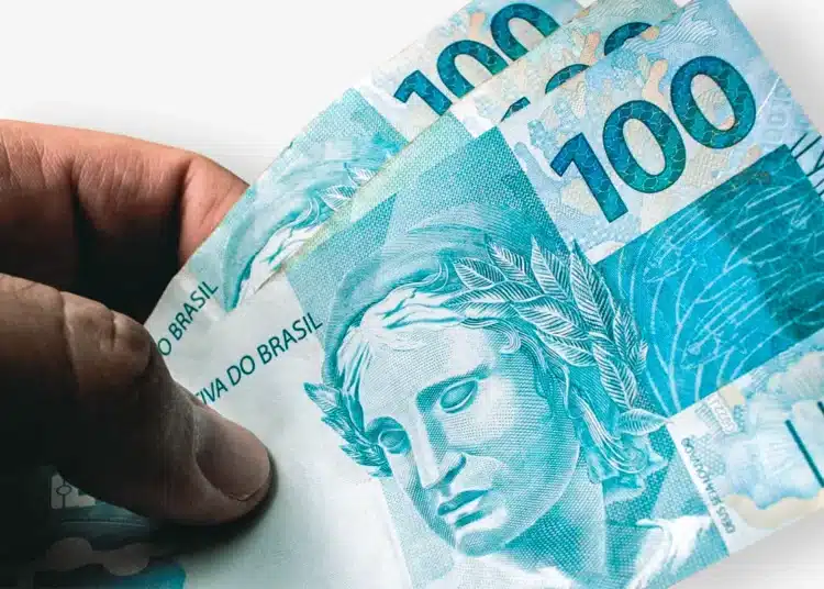 Mão segurando notas de 100 reais com detalhes nítidos do dinheiro brasileiro