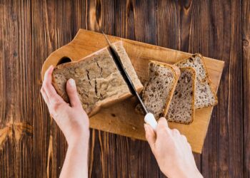 Mãos cortando pão integral em fatias sobre tábua de madeira
