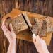 Mãos cortando pão integral em fatias sobre tábua de madeira