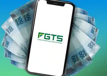 Celular exibindo logo do FGTS apoiado sobre notas de 100 reais em leque
