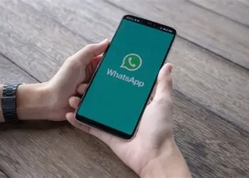 Mãos segurando smartphone com tela do WhatsApp aberta sobre mesa de madeira