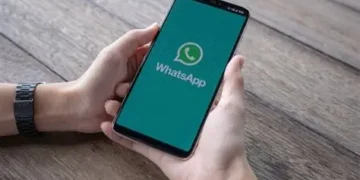 Mãos segurando smartphone com tela do WhatsApp aberta sobre mesa de madeira
