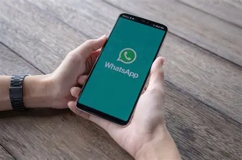 Mãos segurando smartphone com tela do WhatsApp aberta sobre mesa de madeira