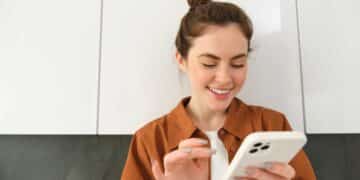 Mulher sorrindo interagindo com smartphone branco em ambiente interno